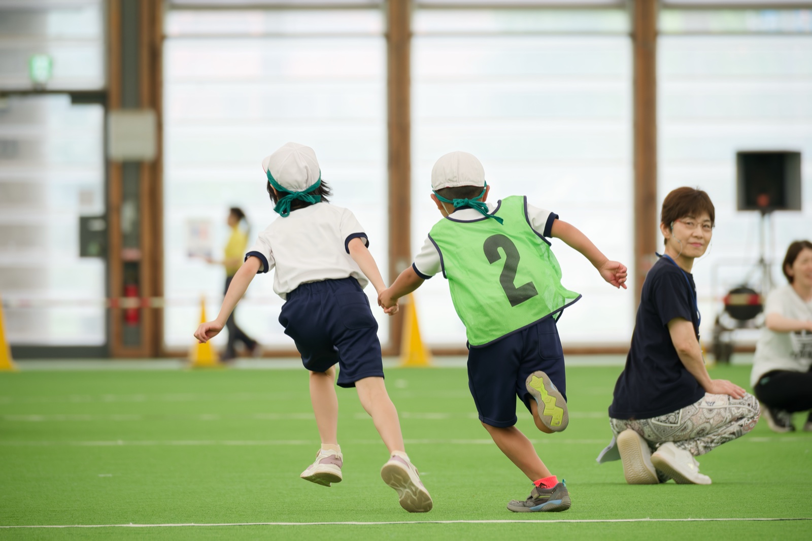 ドーム運動会で友だちと手をつないで走る子どもの後ろ姿（ゼッケン2・DxOで現像）