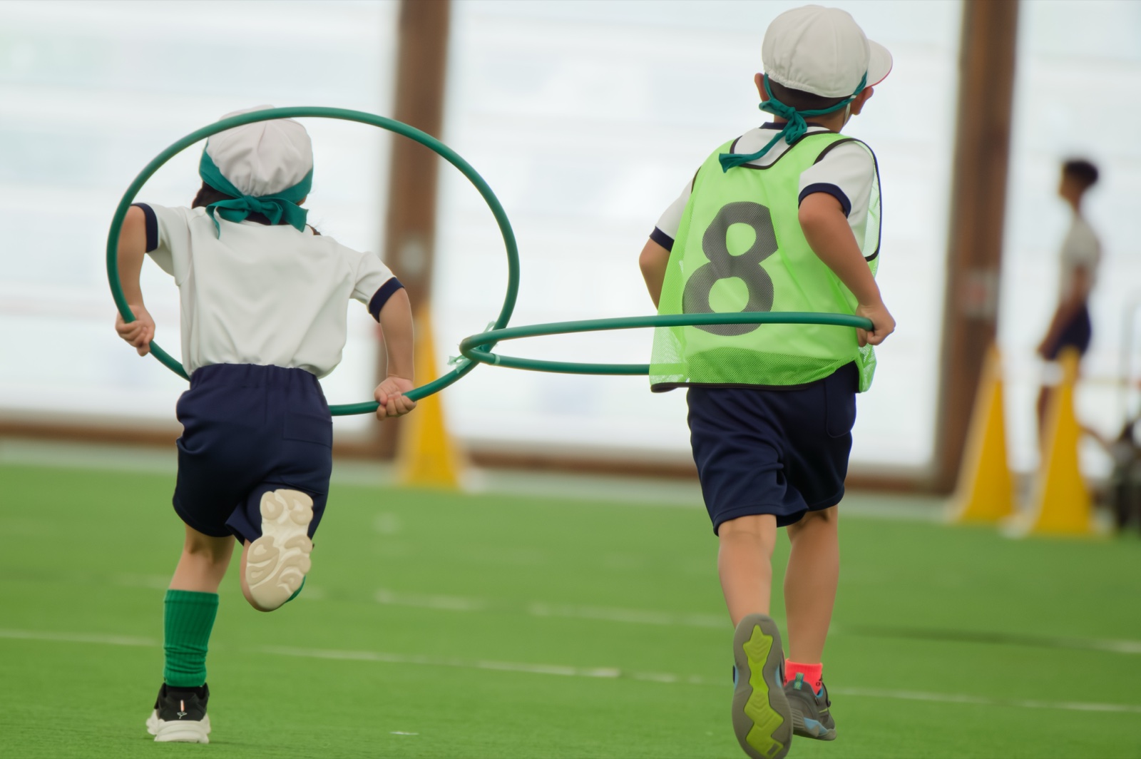 ドーム運動会でフープを回しながら走る子どもの後ろ姿（ゼッケン8・DxOで現像）