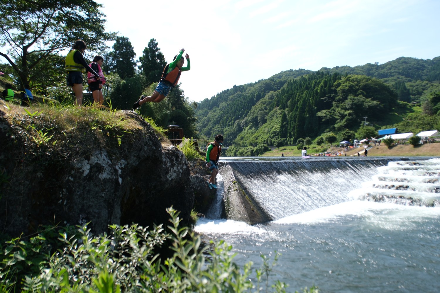 岩の上から川へ飛び込む子ども。下は堰の白い流れ