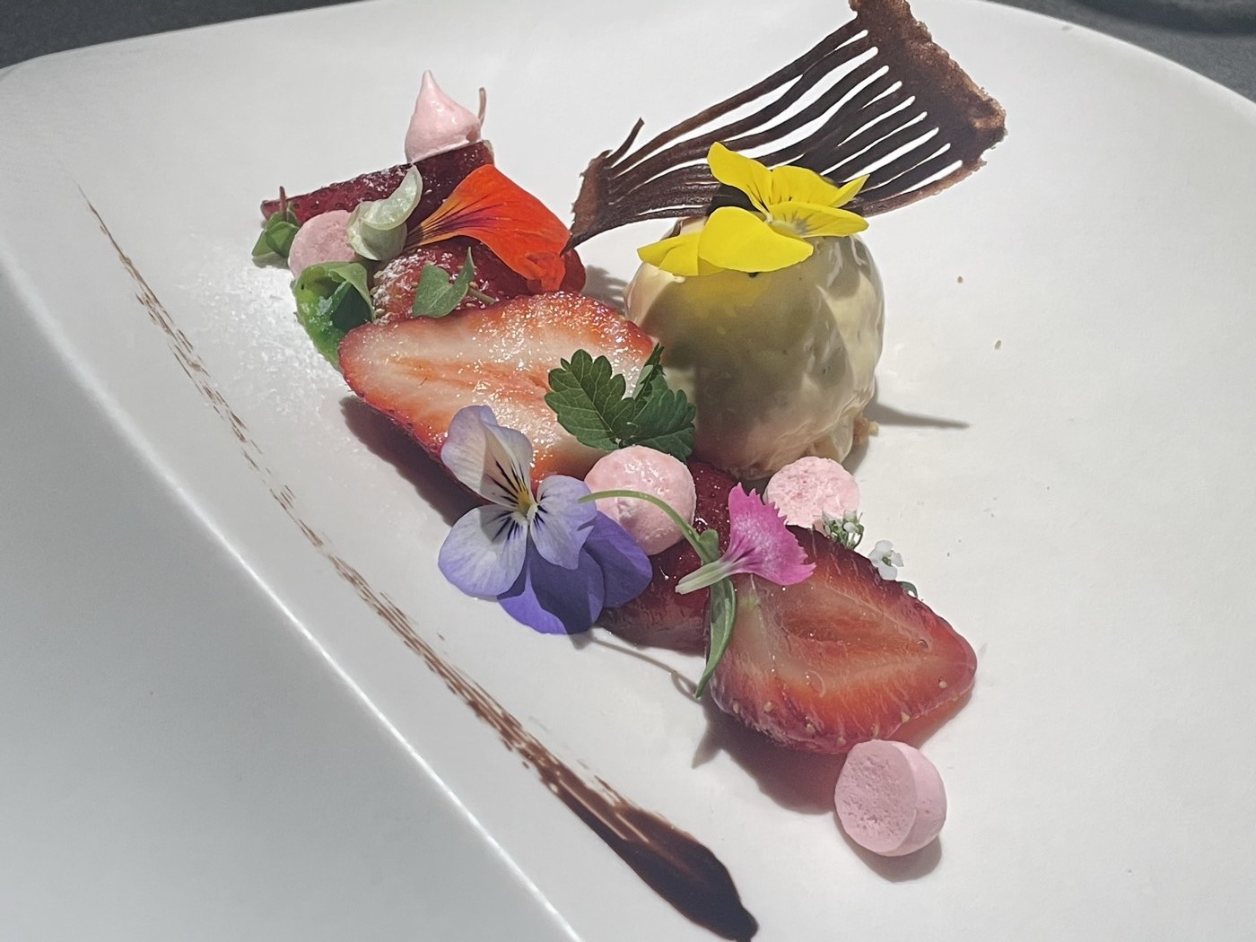 白い皿に苺と食用花、チョコレートを組み合わせたデザート