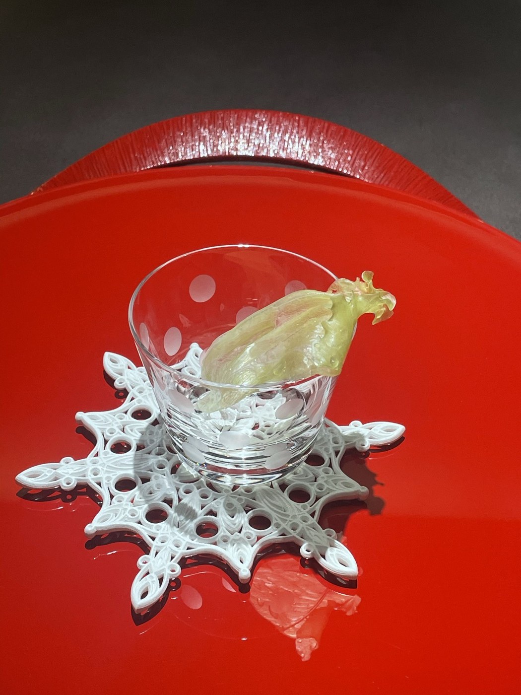 赤い漆の器と雪の結晶の台に置かれたガラスの器に、透き通ったレタスが一枚立ててある