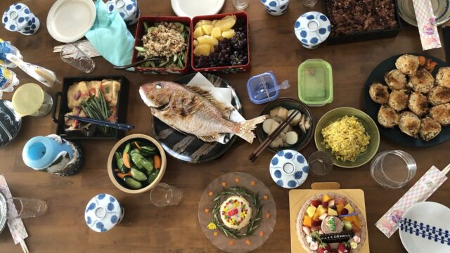 家庭の食卓に、その家のさまざまな器で並べられた料理と鯛の姿焼き