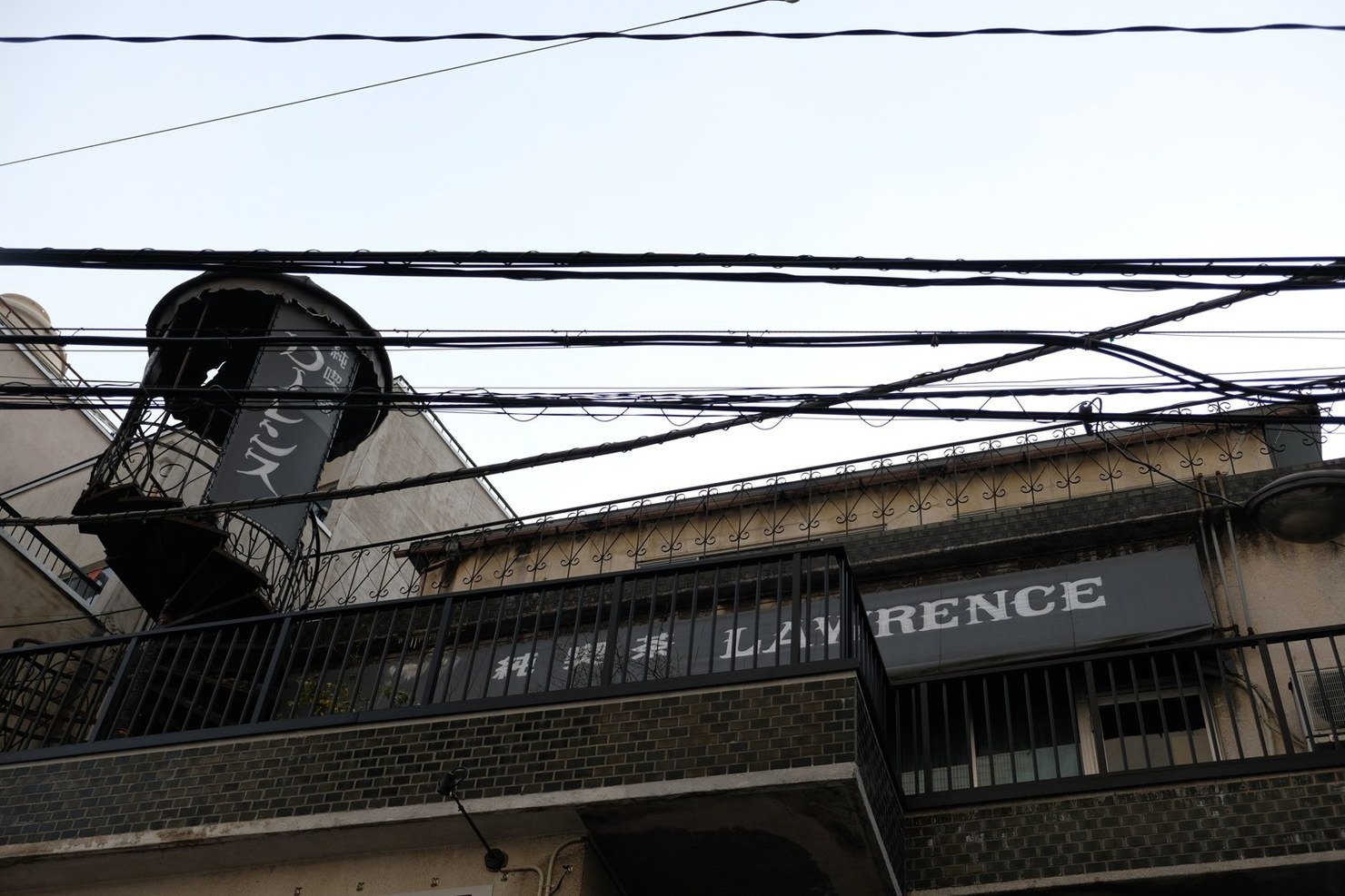 金沢・片町のビルの上に出ている純喫茶ローレンスの看板。横長の看板に「純喫茶 LAWRENCE」の文字、その左に筒型の吊り看板。手前を何本もの電線が横切っている