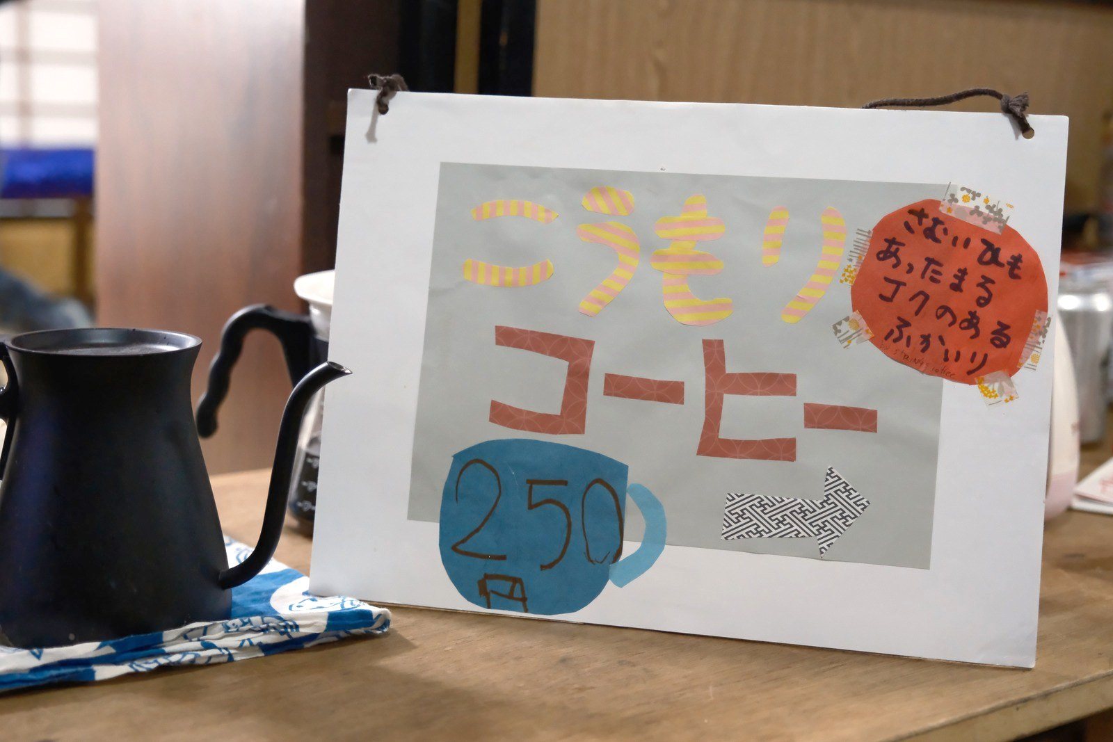 こうもりコーヒーの手書きの看板と、黒い細口ケトル