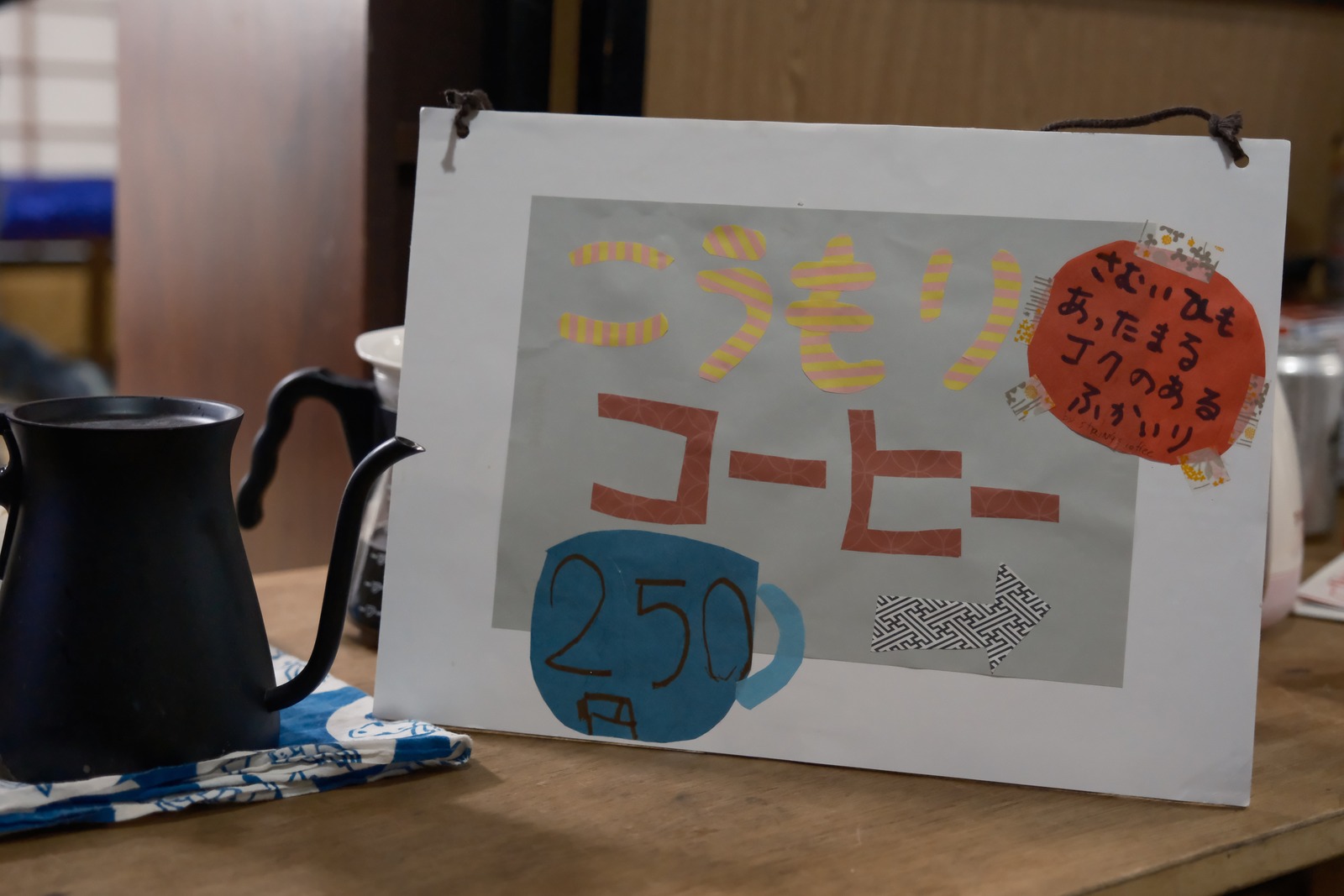 こうもりコーヒーの手書きの看板と、黒い細口ケトル