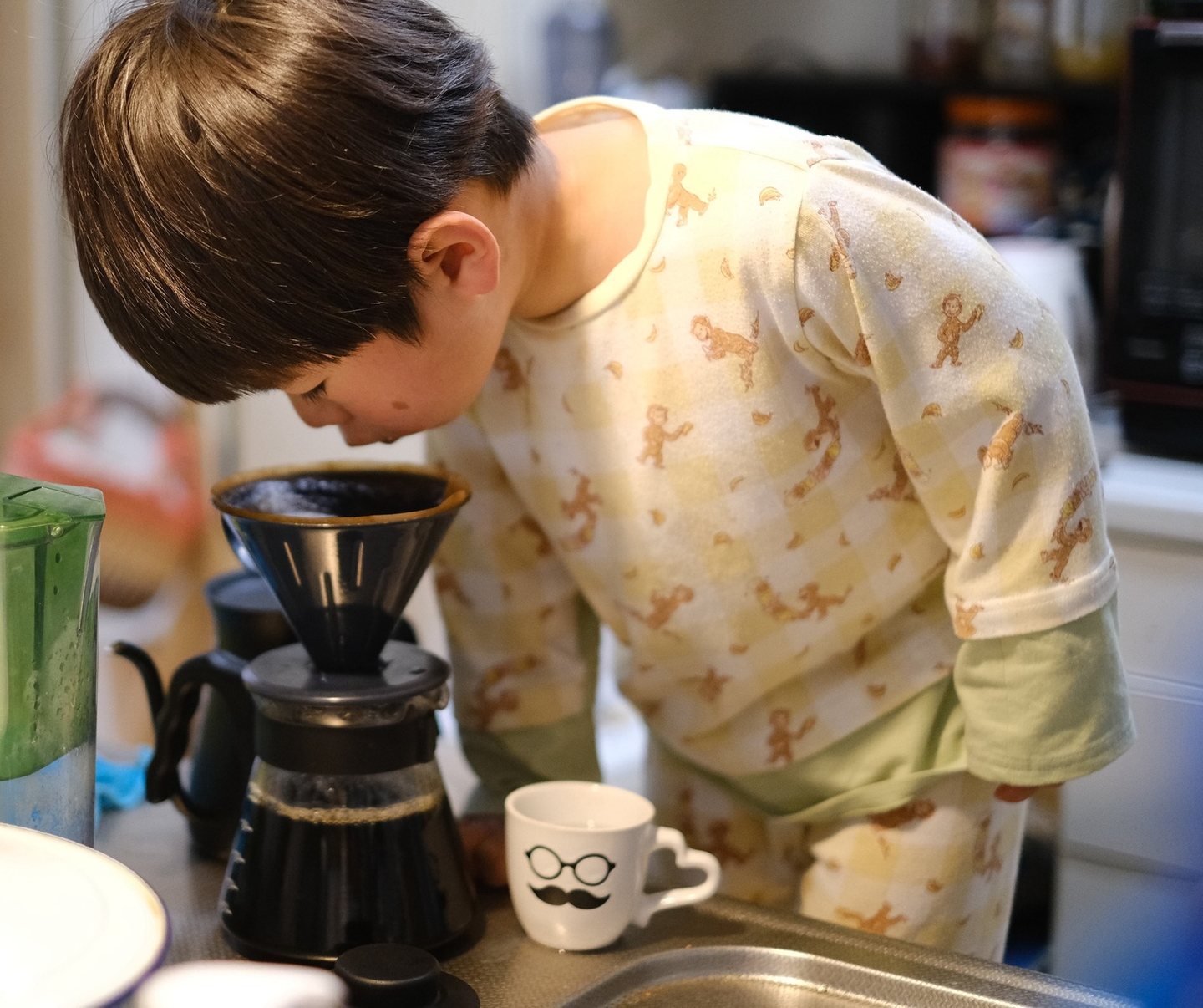 パジャマの子どもが、ドリッパーの上に顔を寄せてコーヒーの香りをかいでいる