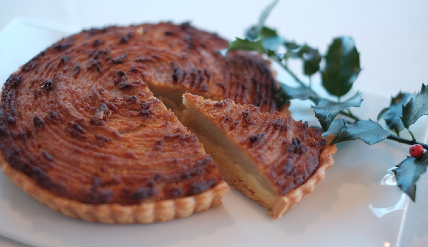 渦巻き模様に焼き色のついたタルト。切り分けた一切れから、黄色い芋のフィリングが見える。ヒイラギの葉が添えてある