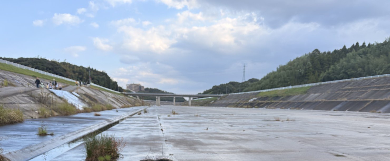 斐伊川放水路の底に降りて撮った、コンクリートの広い水路。両側は斜めの護岸、遠くに小さく人が歩いている