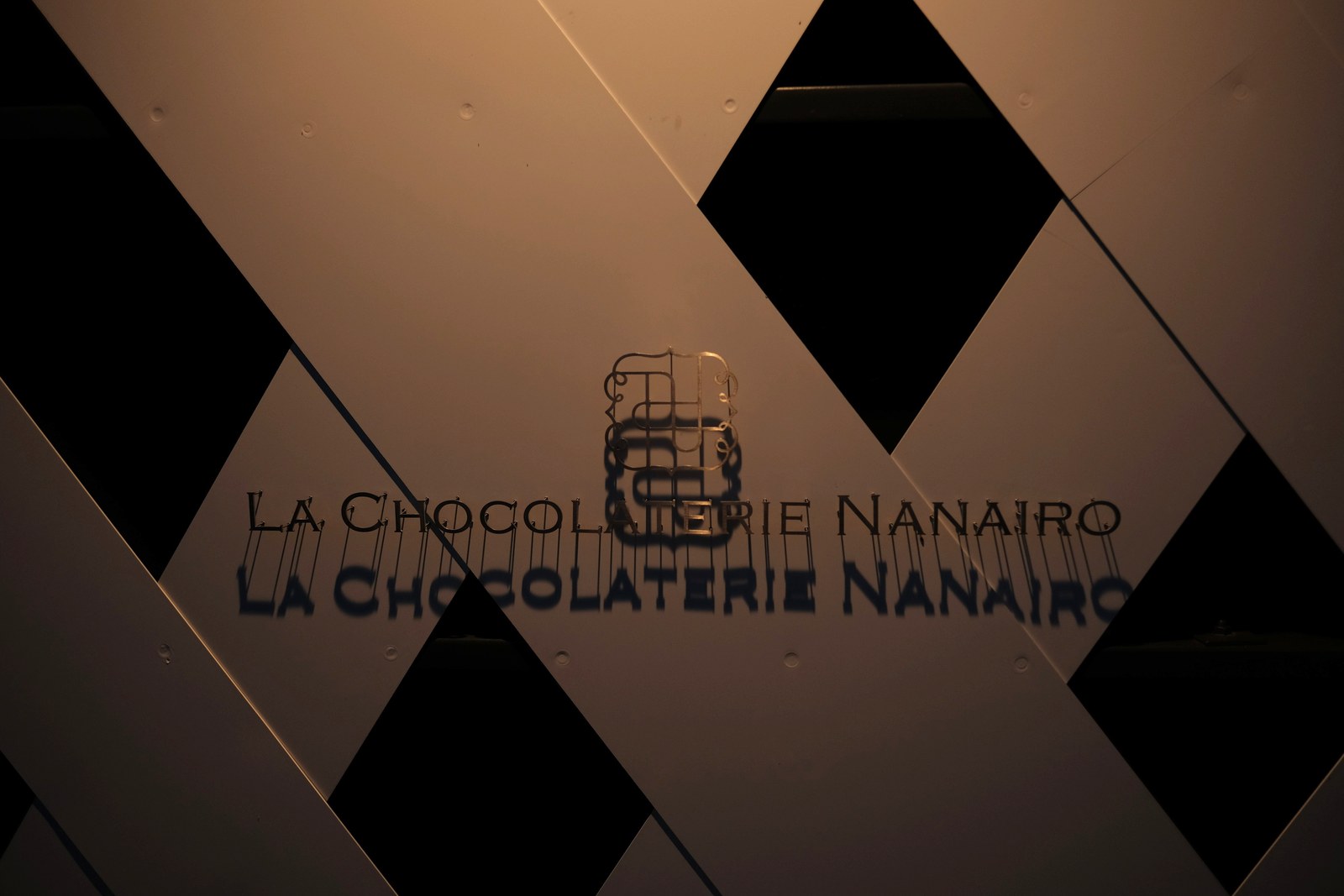 格子模様の壁に、LA CHOCOLATERIE NANAIRO のロゴが浮かぶ、夜のナナイロの外観