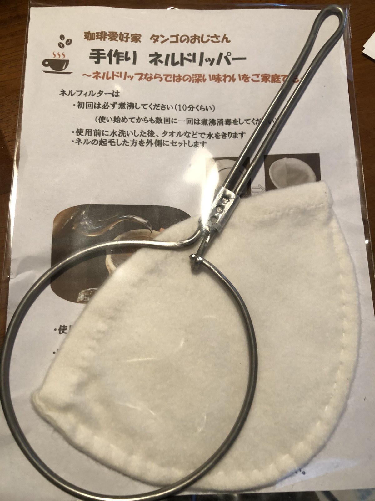 「珈琲愛好家 タンゴのおじさん 手作りネルドリッパー」と書かれた説明の紙の上に置かれた、白いネルと針金の輪