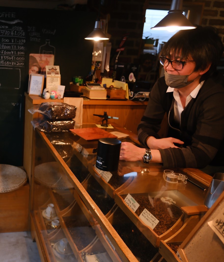 豆のショーケースのあるカウンター越しに笑う、店主の飯島さん。奥に手書きの黒板メニュー