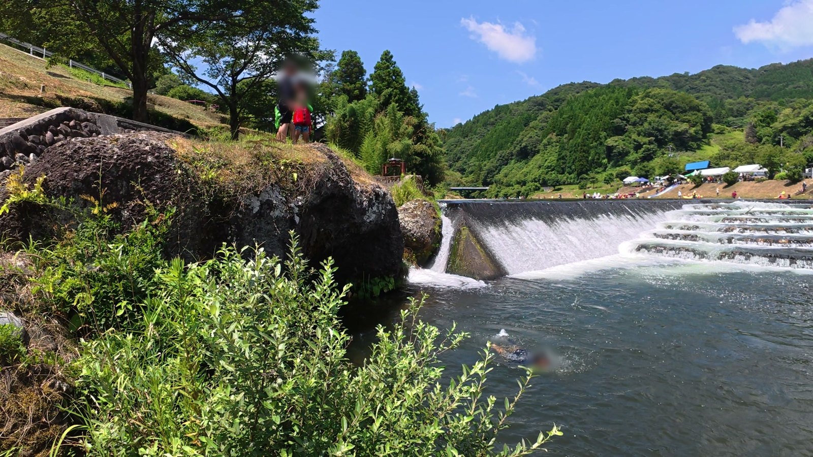 川の堰と岩と夏の山。Osmo Action 5 Pro で水面の近くから撮った1コマ