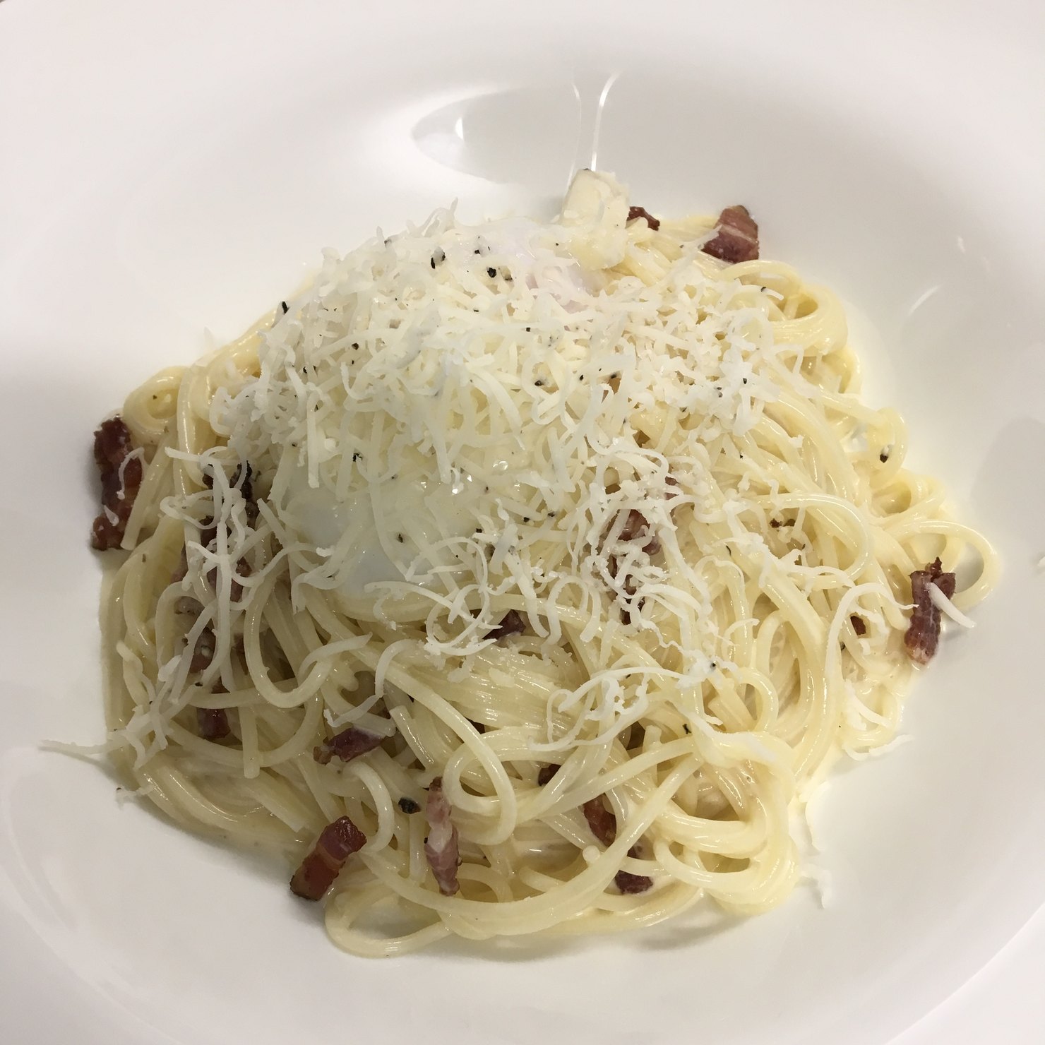 白い深皿に盛った冷製のカルボナーラ。細いパスタの上に、削ったチーズ