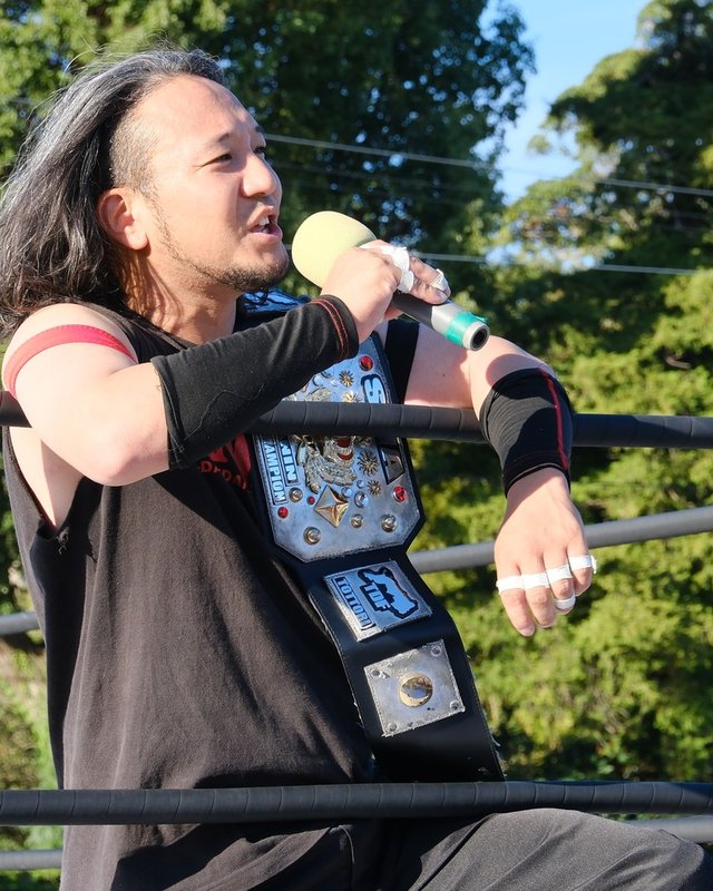 野津朋也選手。ベルトを肩に、マイクで話す