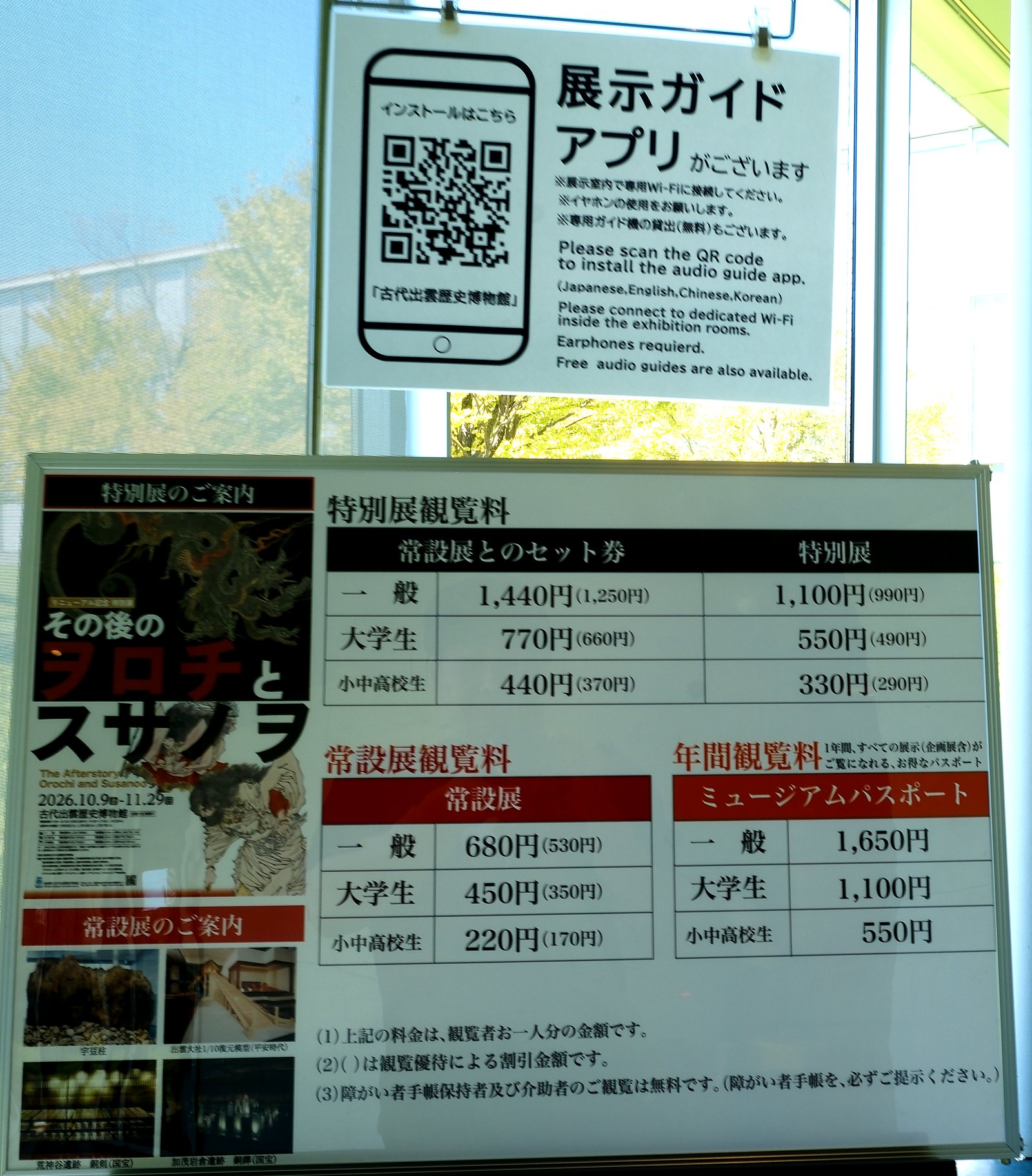古代出雲歴史博物館の入口の案内板。特別展「その後のヲロチとスサノヲ」の観覧料と、展示ガイドアプリの案内(明るさを調整)